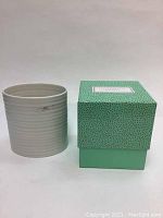 Oval white ceramic vase with horizontal ridges displayed next to the decorative light teal box with speckled pattern.