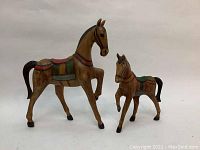 Photo showing two vintage carved wooden horses, one larger and one smaller, both painted with colorful saddles and in used condition without chips.