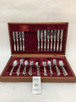 Full open wooden box with red velvet interior holding 15 pieces of silverplated flatware: dinner knives, forks and spoons arranged in two rows.