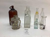 Overview of seven vintage bottles and tobacco jar arranged on white background showing labels and shapes