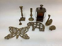 Eight vintage brass decorative items arranged: two candlesticks, a small candle holder, a brass music box vessel, butterfly trivet, turtle trivet, and two small animal figurines (swan and tortoise). Items show patina and use.