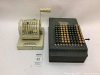 Two vintage mechanical counting machines side by side on a table, showing size and condition contrast