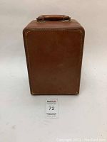 Front view of brown leather carrying case with handle on top, no visible markings or logos.