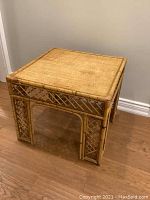 Square vintage rattan accent table photographed from angle showing lattice sides and legs with some missing interwoven pieces on legs.
