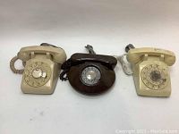 Three vintage rotary telephones in beige and brown colors, showing signs of wear and stains.