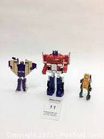 Photo showing all three Transformers toys: Optimus Prime in center, purple and beige Decepticon to left, yellow and green Autobot to right