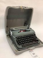 Vintage Olympia manual typewriter inside open gray hard case with green handle and chrome clasps.