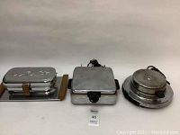 Front view of three vintage waffle makers on white background.