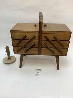 Straight front view of closed wooden 3-tier sewing basket with legs and handle