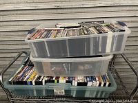 Three clear plastic bins stacked, filled with over 200 DVDs visible from top and side angles.