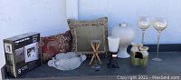 Photo showing decorative pillows, boxed digital picture frame, frosted glass and metal candleholders, small cache pot type vase, large white textured vase, and two tall glass candleholders with gold accents.