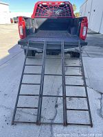View of the ramp unfolded and positioned leaning on truck bed, showing full length and width with open tubular metal construction.