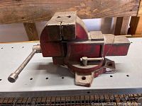 Side view of red bench vise showing handle and fixed base.