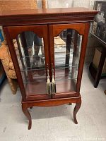 Front view of a wooden curio cabinet with glass doors and display shelves inside, standing on curved legs.