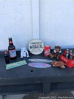Photo of entire lot showing all bottles, signs, and stuffed animals on black table against white wall.