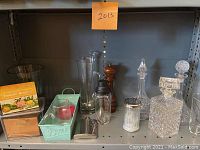 Shelf with copper recipe box, large glass vase, tall glass pitcher with stirring rod, pepper grinder, metal flask, crystal decanters.