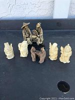 Seven small oriental figurines on a dark surface showing their overall size and grouping