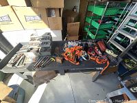 Overview of lot displayed on black folding table including hand tools, tie down straps, ropes, and toolbox.