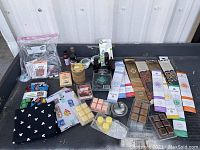 Photo of entire lot including fabric bolts, incense packs, wax melts, oils, and sewing needles and thread bag on a black surface