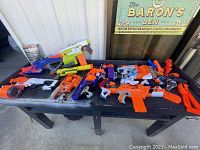Collection of various Nerf toy blasters and parts on black table.
