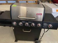 Overall front view of the Outdoor Gourmet gas grill with six knobs and side shelves, showing condition and general appearance