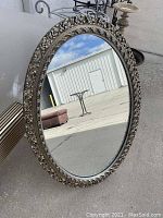 Front view of the oval mirror showing the reflective glass and decorative carved frame with floral and vine patterns in off-white and natural wood colors.