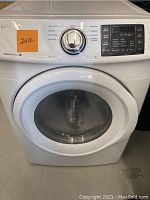 Front view of white Samsung electric dryer with control knob and digital display panel, showing various drying cycle options and the year sticker 2012.