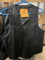 Front view of black leather vest size 38 hanging on blue hanger with post-it note showing number 2030.