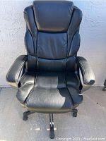 Front view of black padded Staples office chair showing cushioning on seat, backrest, and armrests.