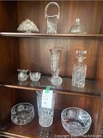 Full display of assorted crystal items on a wooden shelf showing vases, candy dish, napkin holder, butter dish