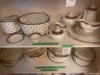 Protective fabric covers holding stacks of plates and bowls with teapot, coffee pot, cream jug, sugar bowl, gravy boat on tray visible