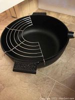 Black round cast iron pot with metal rack insert inside, shown on tile floor.