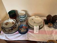 Four dark green rice bowls at left, five assorted white and patterned rice bowls stacked center, and two multicolor decorative bowls on floral plates front left.