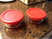 Two small Pyrex round glass bowls with red lids shown on countertop
