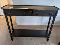 Front view of black hallway table showing two drawers with ring pulls, bamboo-style legs, and a lower shelf.