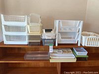 Wide view of assortment of white, cream, clear, green, and black plastic storage bins and organizers of multiple sizes and types on wooden shelves.