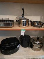 View of Lagostina pressure cooker, roasting pans, stock pot, double boiler with poacher, showcasing stainless steel and black speckled enamel finishes.