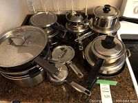 Assortment of pots and pans with lids and black handles displayed on kitchen counter.