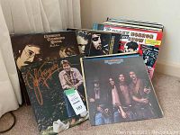 Front view of leaning vinyl LPs against wall; shows John Fogerty cursive cover, CCR Pendulum and unseen titles in stack