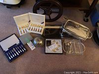 Full lot shot showing boxes of gold spoons, appetizer forks, chafing dish, glass serving tray with utensils, and trays