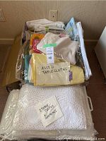 Photo showing plastic bag with assorted colorful fabric table cloths and a bag with white crocheted cloths and napkins.