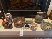 Front view of eight ceramic items displayed on mantle: three vases, decorative bowl, jug, rectangular ashtray, and two round bowls including ashtrays.
