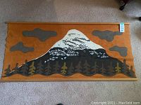 Full front view of the wall hanging showing mountain, trees, animals, clouds, orange background, mounted on wooden rods.