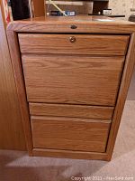 Wooden filing cabinet closed, showing three drawers with one locking drawer but no key.