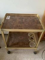 Top view of brass trimmed beverage cart showing the woodgrain finish on the top surface with brass edges and four casters visible.
