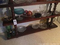 Wooden shelf displaying various crystal bowls and glass decor items including colored glass spheres and blue frosted pedestal bowl.