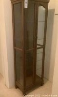 Tall wood framed curio cabinet with glass doors and glass shelves inside, viewed at an angle showing front and side glass panels.