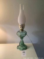 Full view of the glass hurricane lamp showing the green glass base, brass burner, frosted chimney, and clear glass tubes on top.