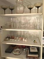Shelves filled with assorted glassware including coupe glasses, clear small glasses, salt and pepper shakers, and plates.