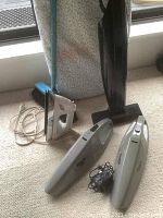 Sunbeam iron next to Bissell Featherweight vacuum and two Shark cordless dusters on floor near window.